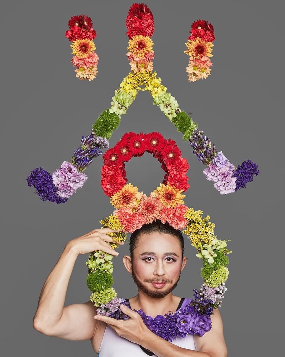 赤・黄・紫の花で大きな文字を組んだ髪飾りを、頭に載せた出演者